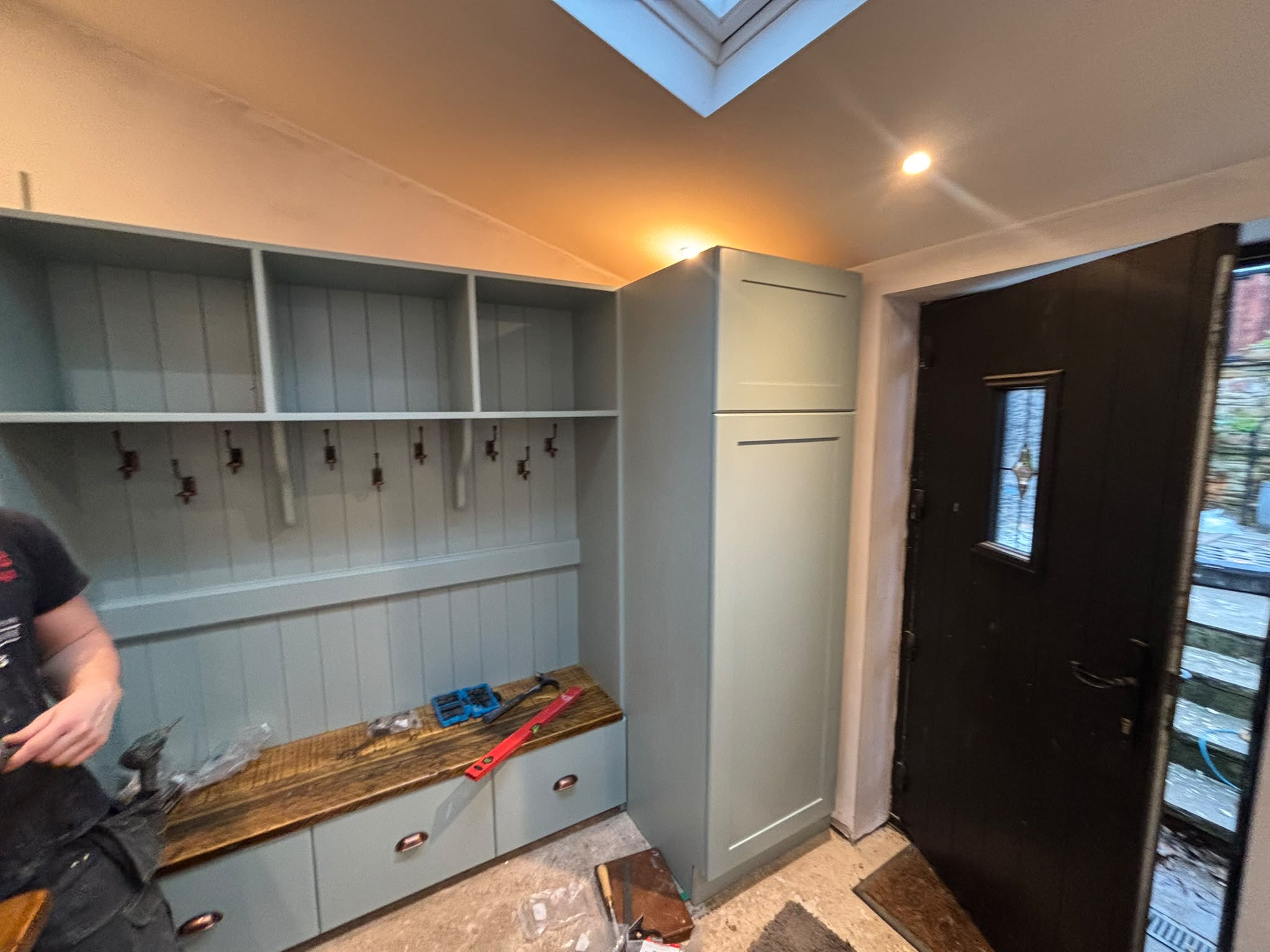 Bespoke fitted boot room cabinet hand-painted sage green with open shelving, coat hooks, a reclaimed oak bench seat and a full-height cupboard — Oak & Pine by Design, Yorkshire