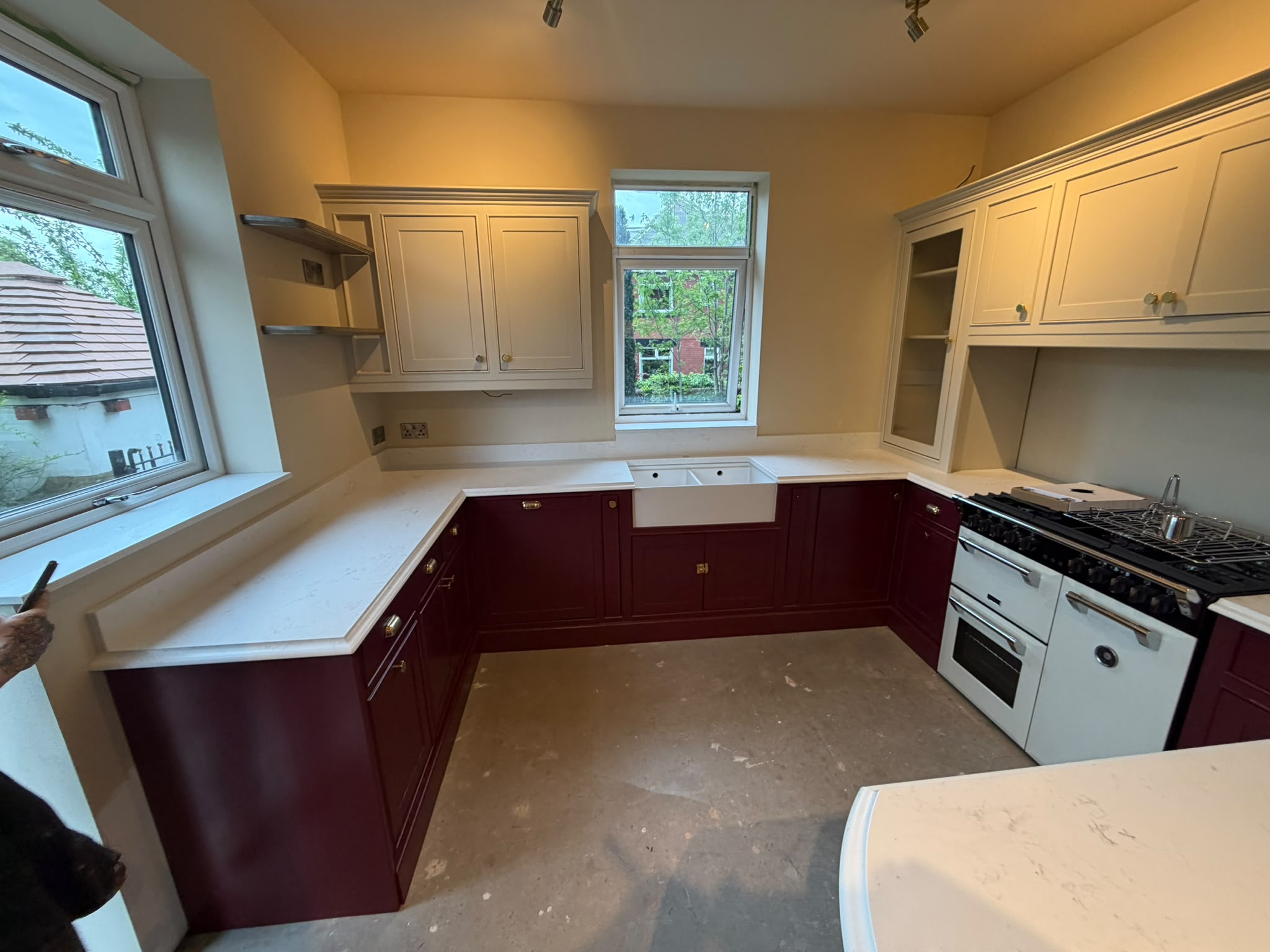Handmade two-tone Shaker kitchen in an L-shape layout, painted claret and cream with brass cup pulls, marble worktops, range cooker and a Labrador in shot for scale — Oak & Pine by Design, Yorkshire