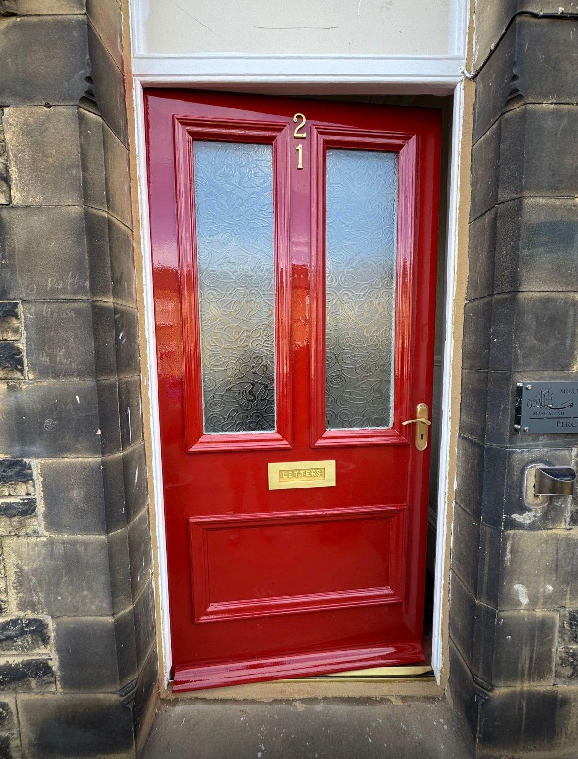 Restored Victorian front door finished in gloss red with brass letterplate and door furniture in a stone surround, Yorkshire