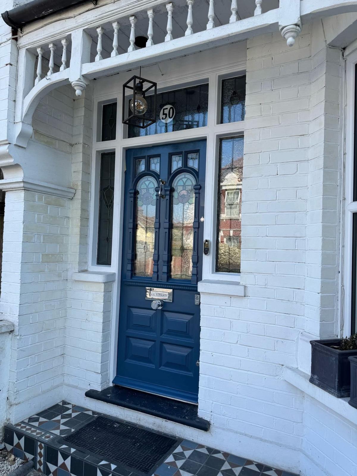 Restored Victorian stained-glass front door in navy set in a tiled porch with timber balustrade, Yorkshire